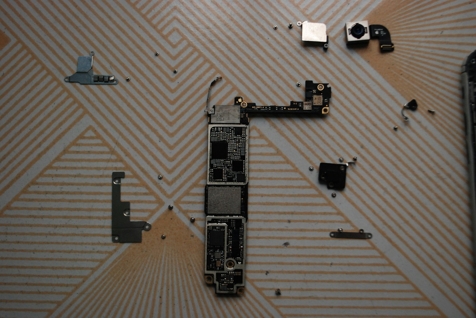 Placa, câmeras e pequenos componentes de um smartphone organizados sobre a mesa